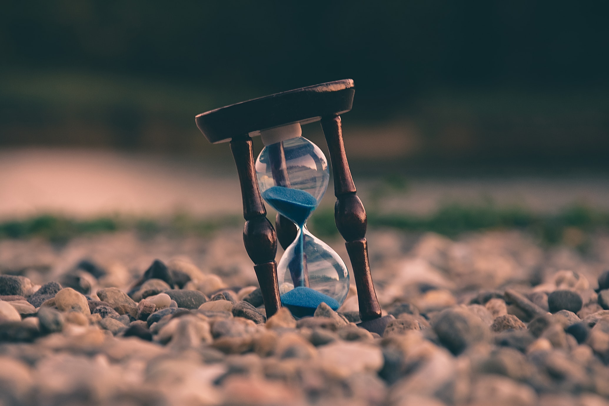 Closeup of an hourglass, half consumed, sitting on a bed of gravel.