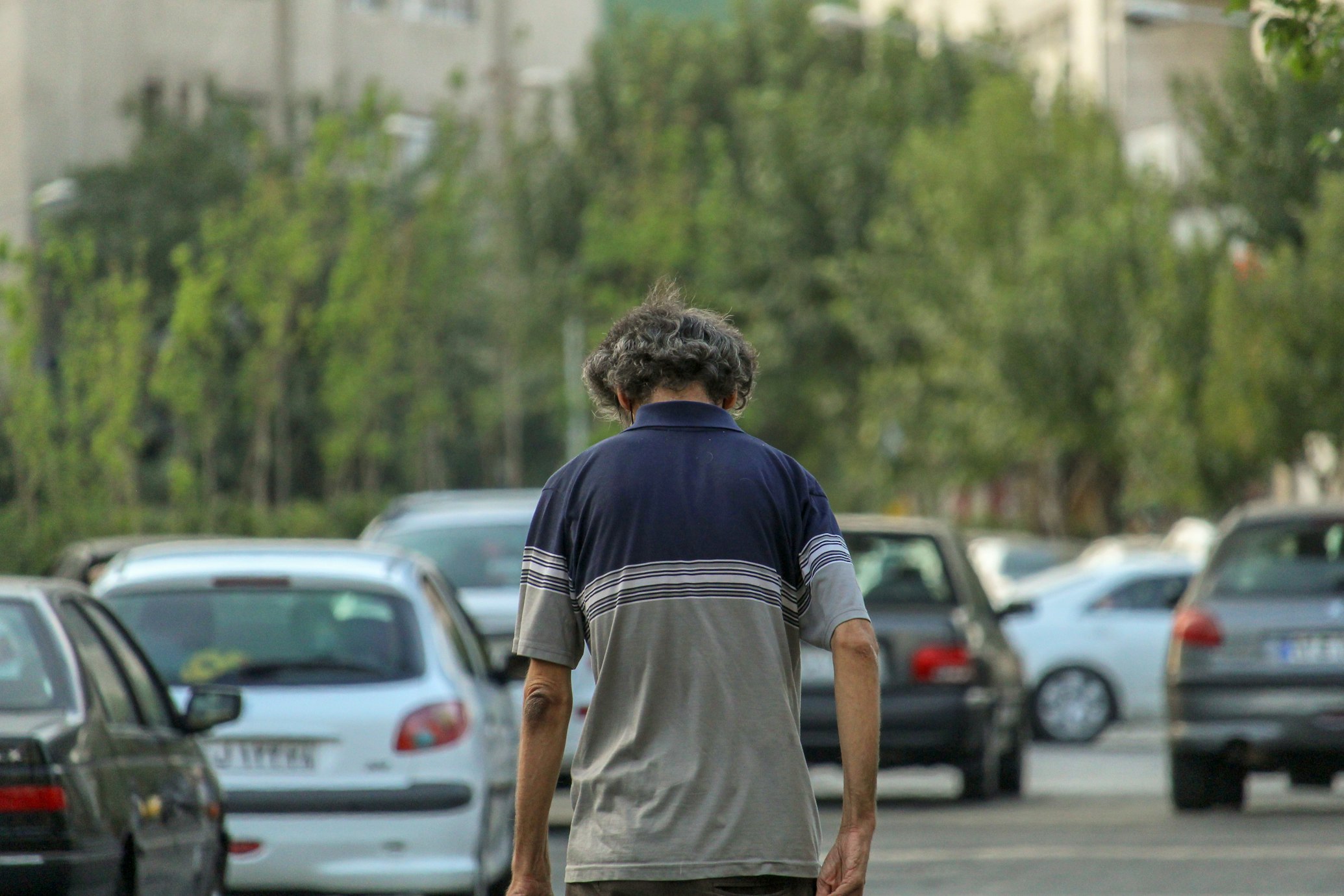 Photo of a man walking in a long line of cars with his head and shoulders slumped