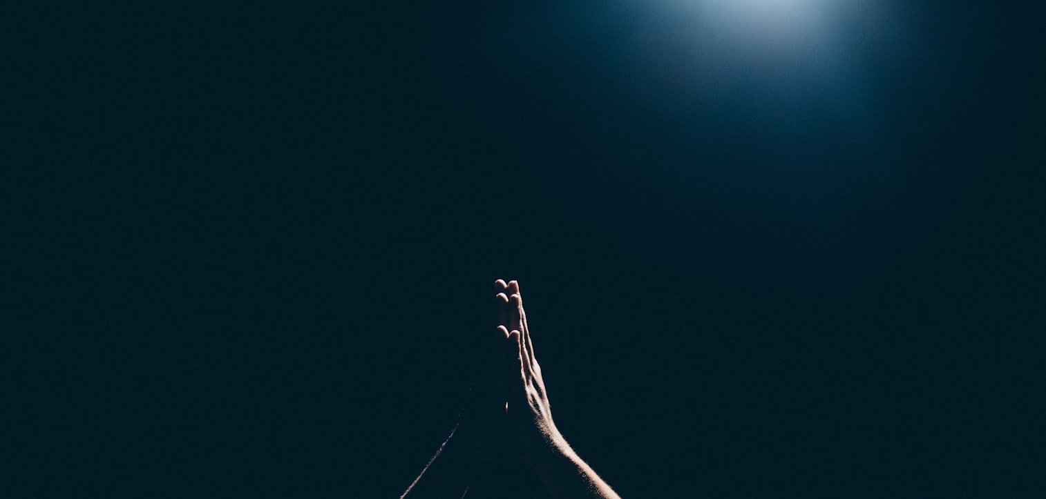 Hands raised in prayer against a dark sky